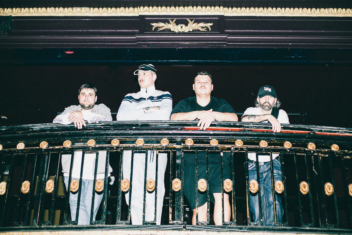 Australian rock band Trophy Eyes band members standing together and leaning on an ornate balcony railing inside a dark concert venue.